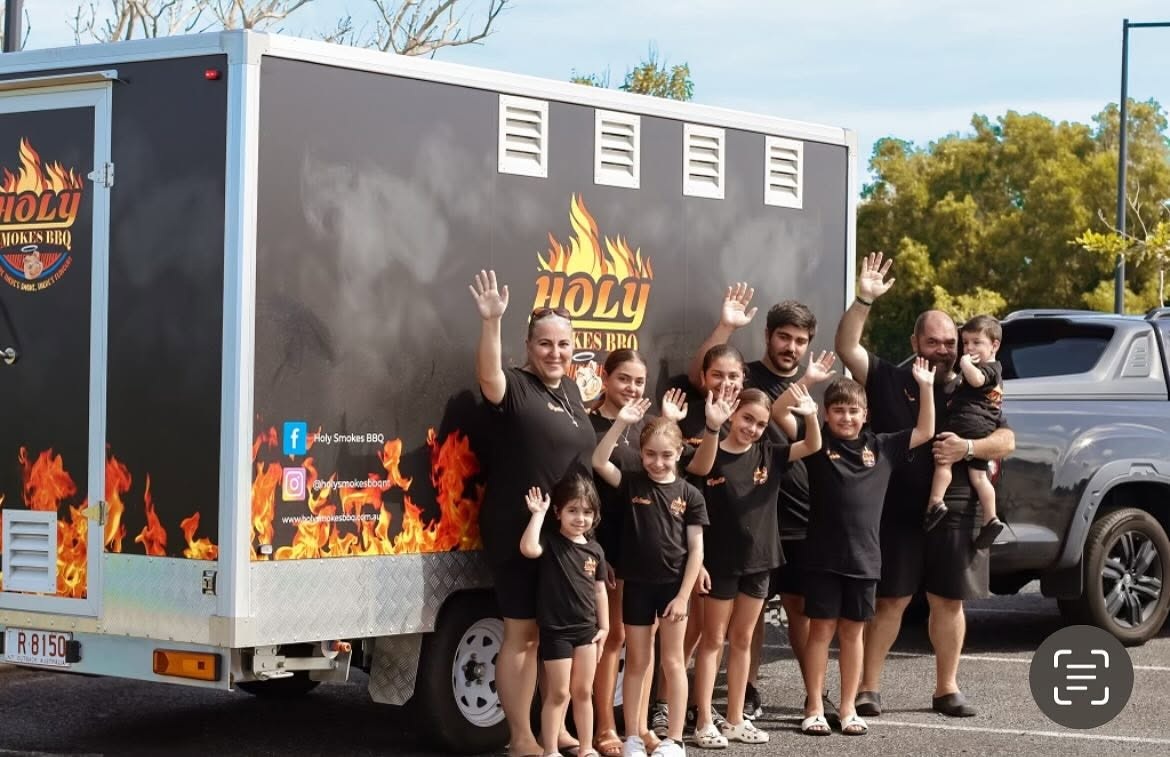 The Holy Smokes family waving together beside their BBQ trailer